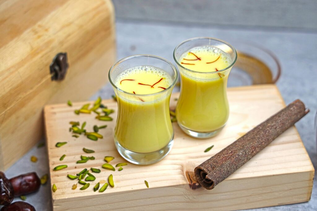 Turmeric and saffron milk on a rustic wooden board, garnished with pistachios.