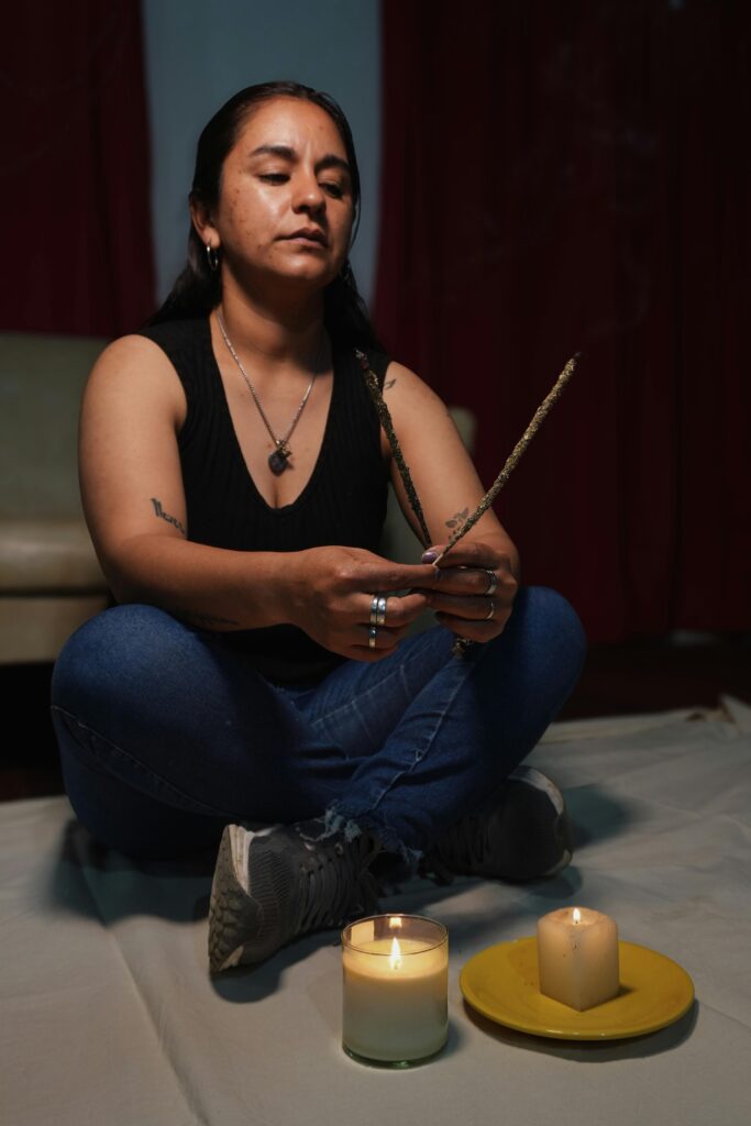 Woman meditating with candles and incense indoors, conveying calmness.