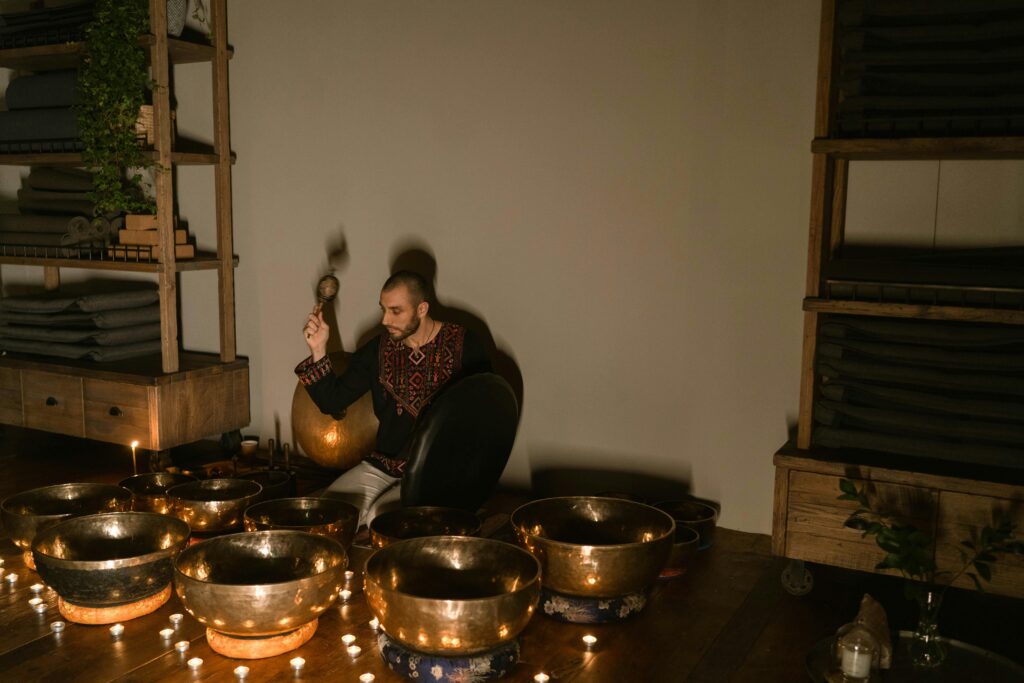 A serene indoor setting with a man playing Tibetan singing bowls surrounded by candles, promoting relaxation and mindfulness.